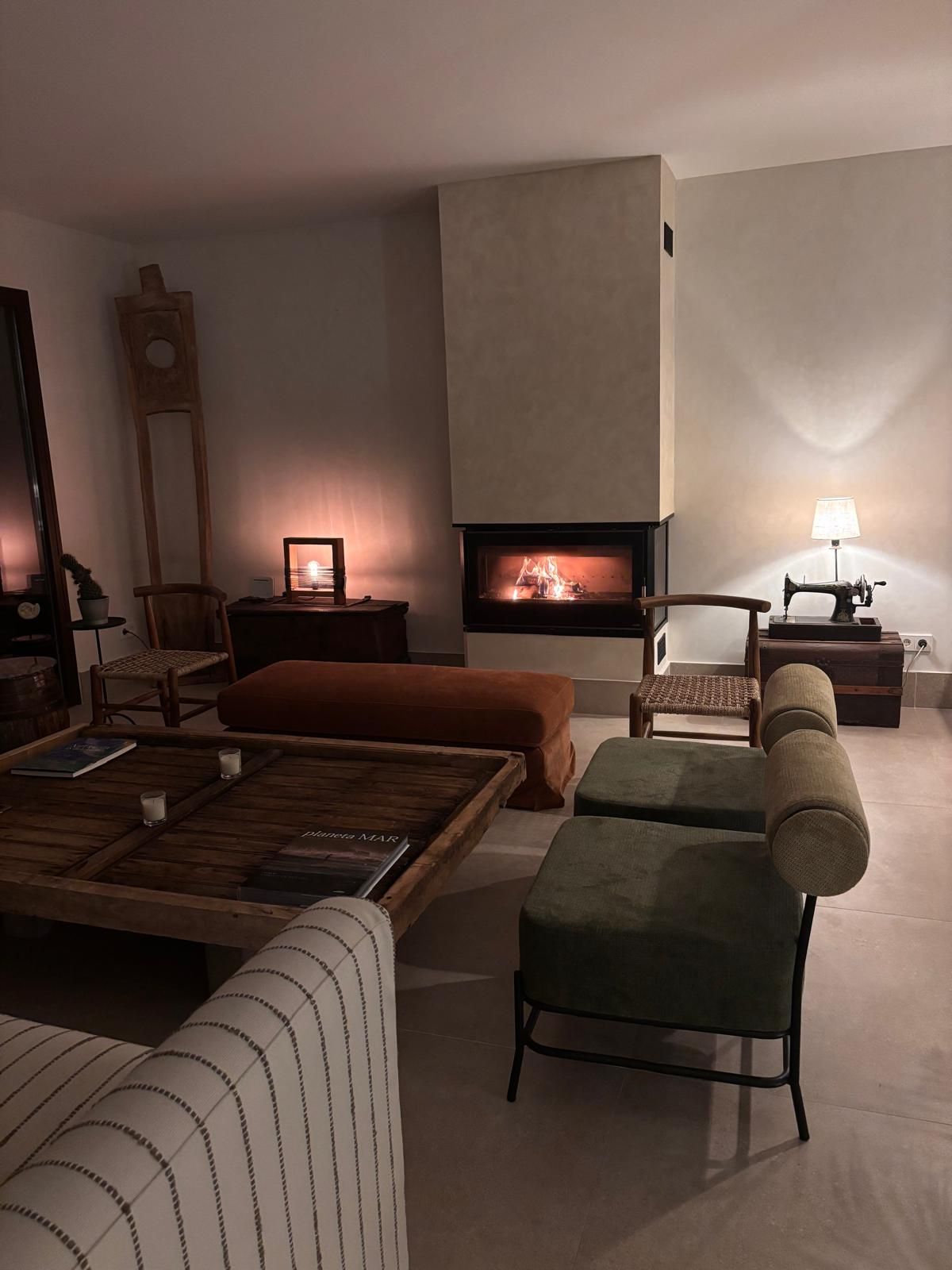 Acogedora sala de estar con sofás, mesa de centro, lámparas y una chimenea encendida en una noche oscura.