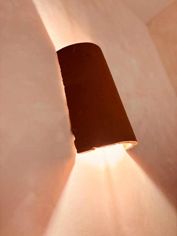 Aplique de pared marrón que proyecta una luz cálida sobre una esquina de pared beige.