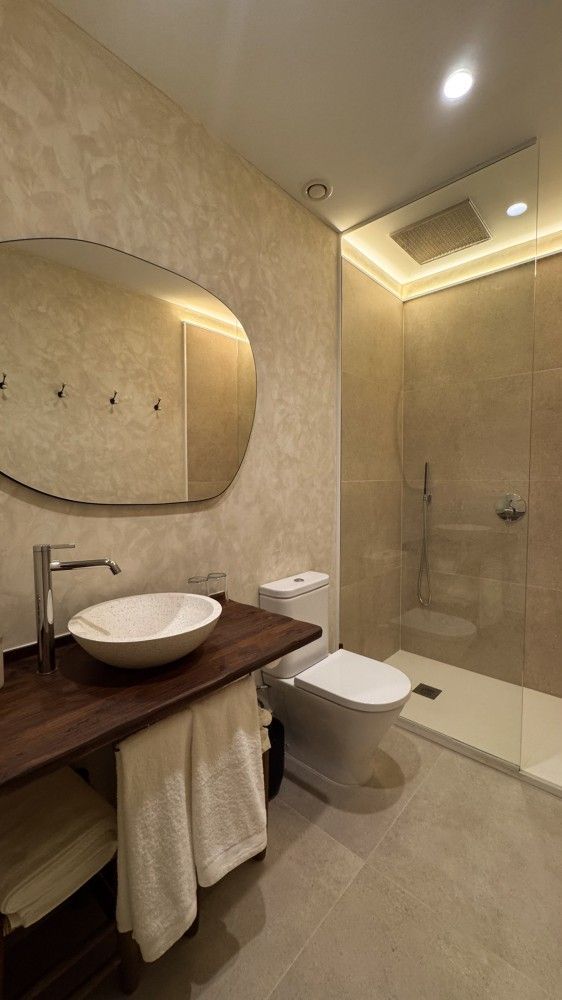 Baño moderno de color beige con lavabo, espejo, inodoro y ducha de cristal.