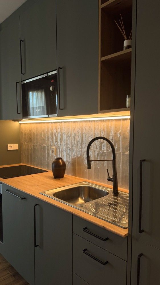 Cocina moderna con gabinetes oscuros, salpicadero iluminado, fregadero, grifo negro y encimera de granito.