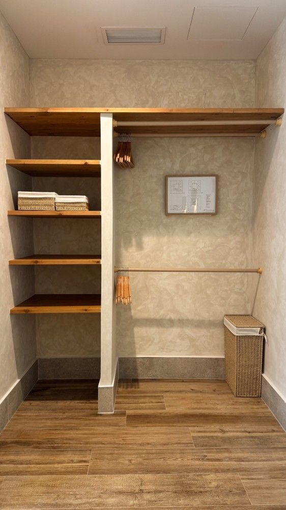Vestidor vacío con estantes de madera, barra para colgar ropa y suelo de madera bajo una pared de color beige.