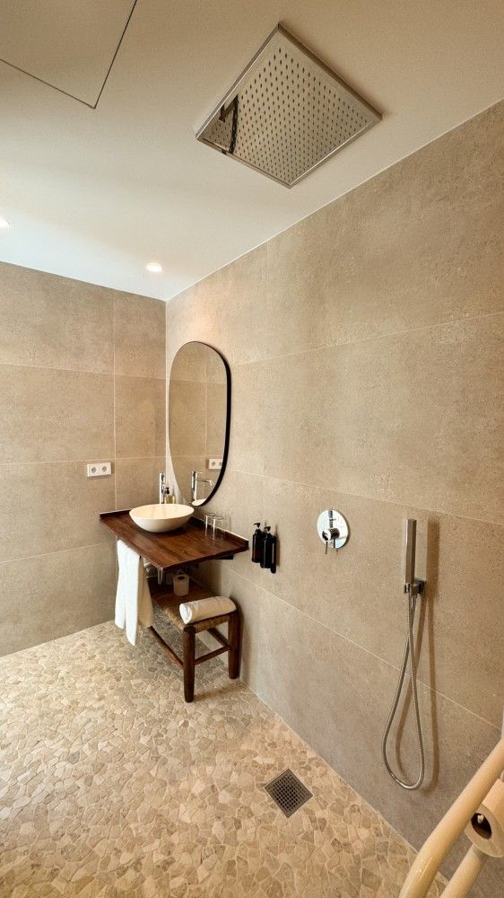 Baño minimalista con paredes de color beige, lavabo mural, espejo y cabezal de ducha.