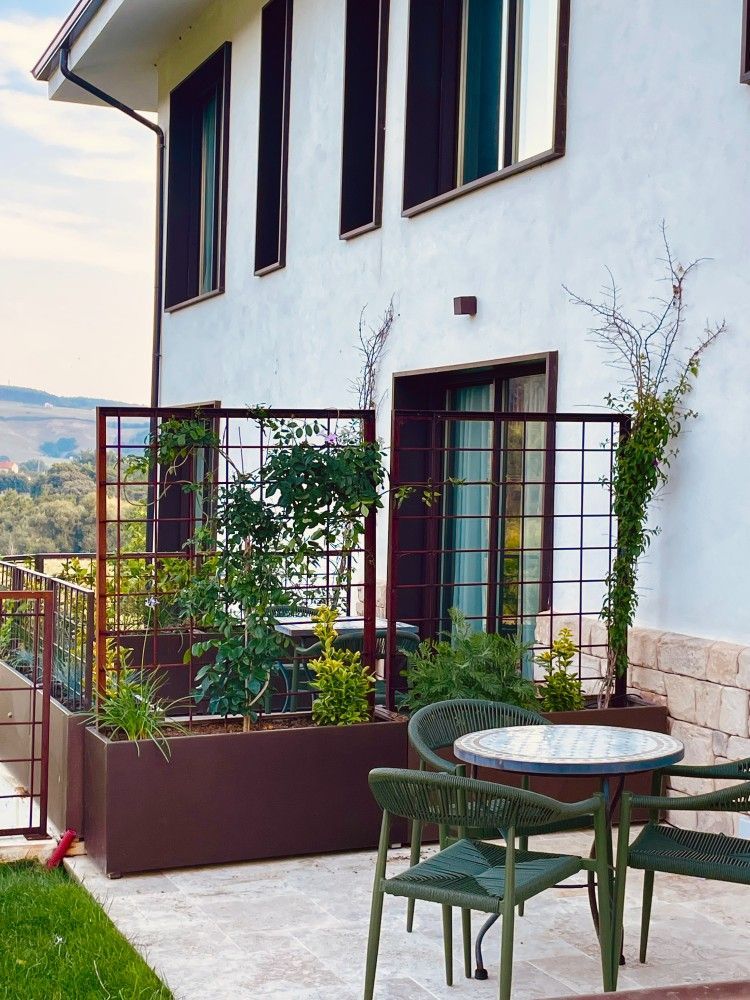 Patio de la casa con sillas verdes y mesa redonda junto a un edificio blanco y plantas en macetas.