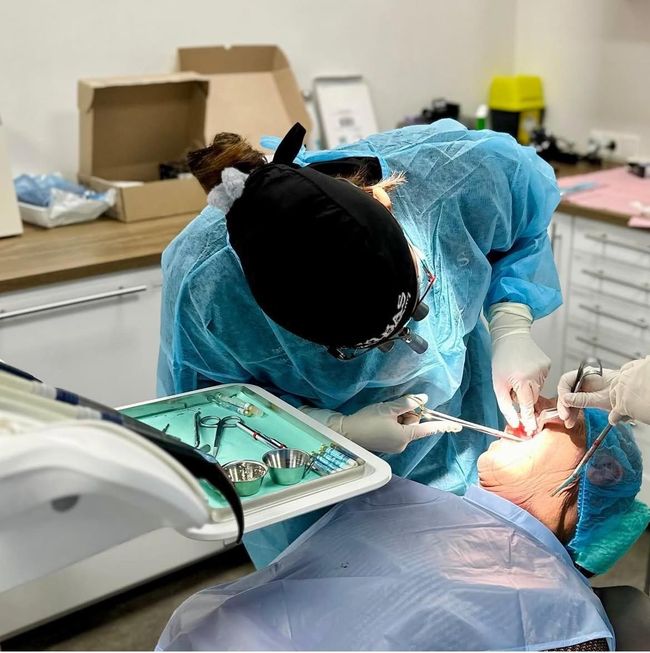 Tandarts in blauwe beschermende kleding voert een tandheelkundige ingreep uit bij een patiënt in een kliniek.