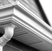 Close-up of a house gutter and ornate white downspout under the roof eaves.