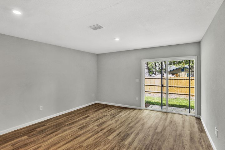 Empty room with wood floors, gray walls, and sliding glass door to backyard.