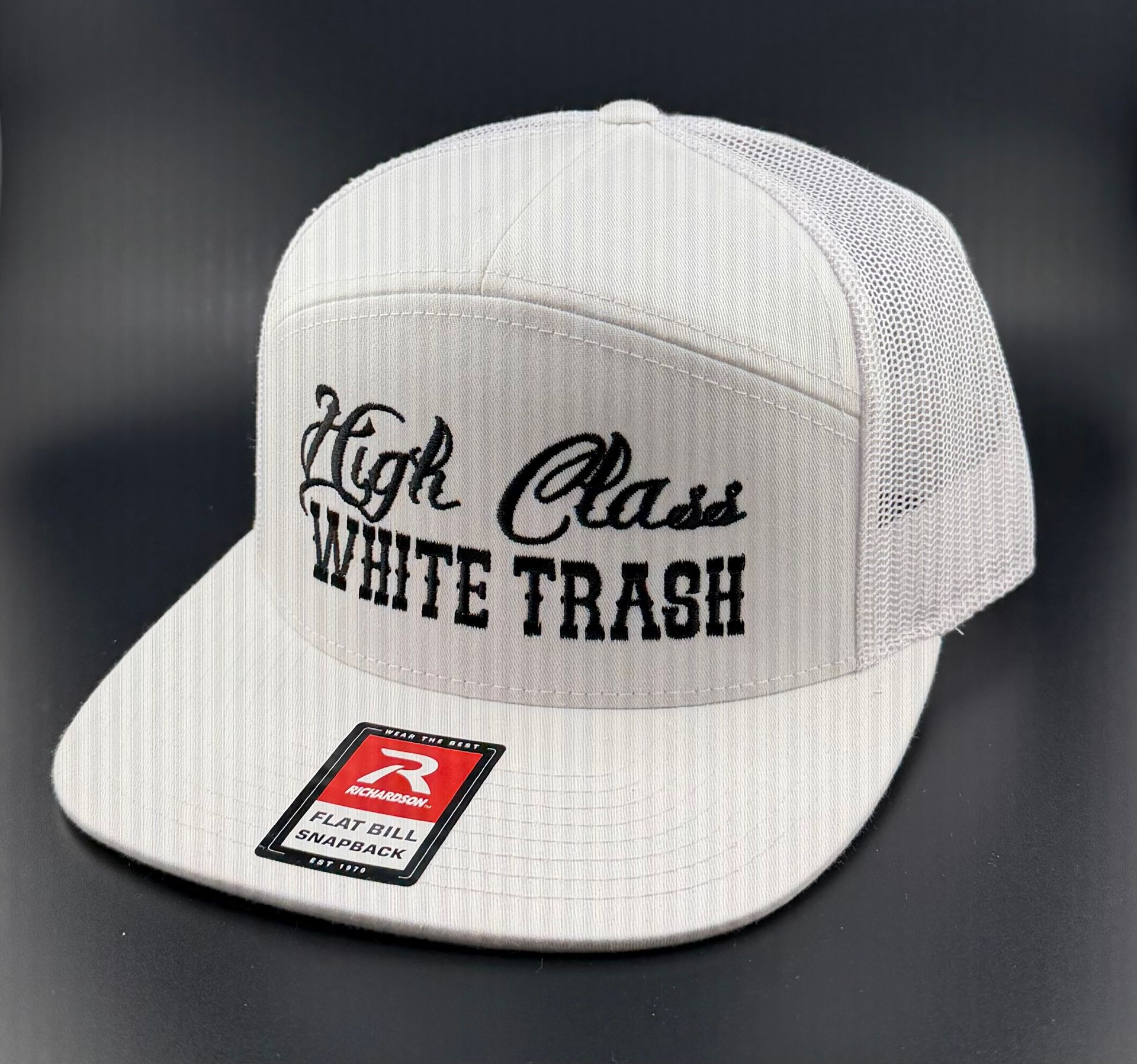 A white mesh-back trucker hat with "High Class WHITE TRASH" embroidered in black text on the front and a brand sticker.
