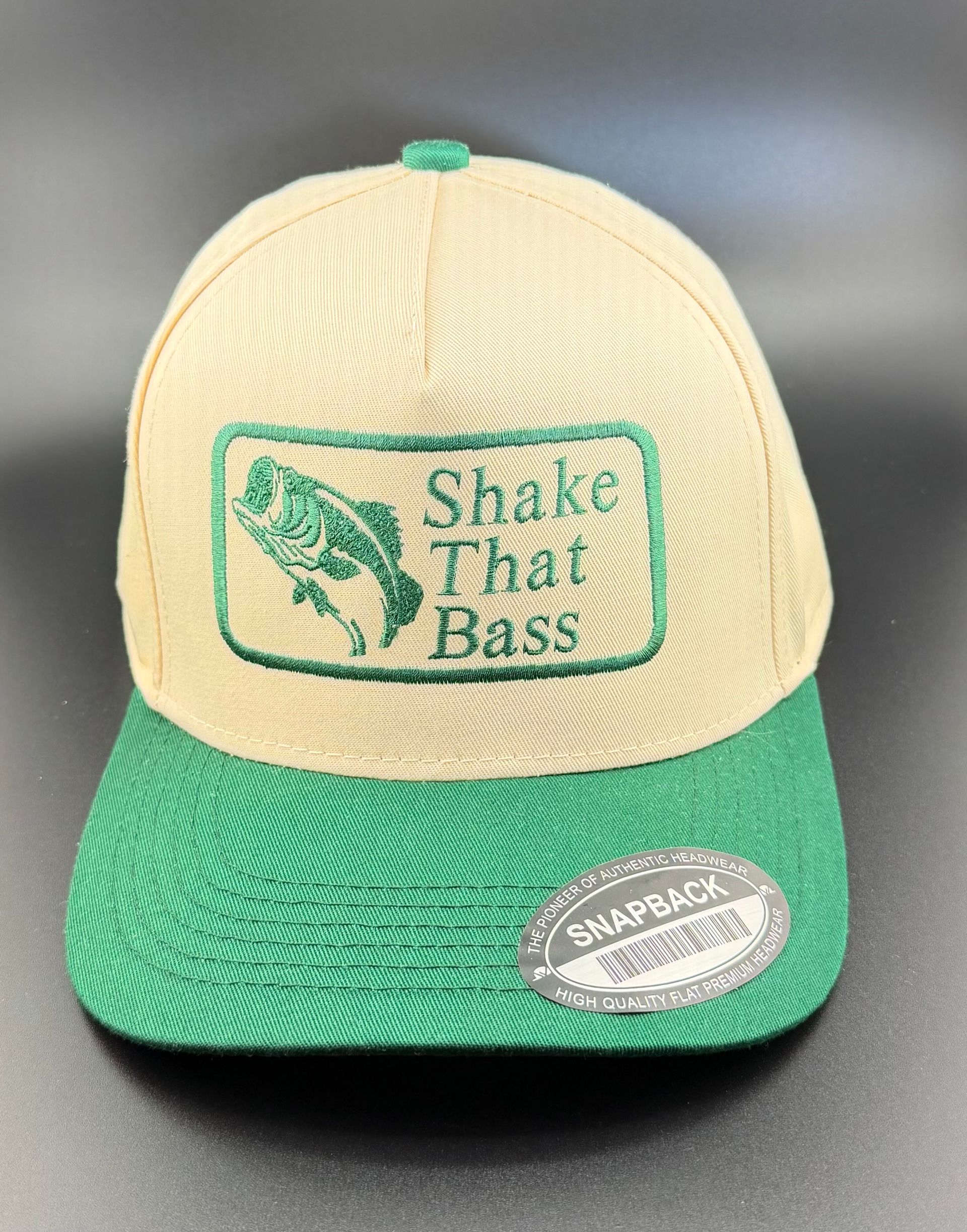 A tan and green snapback cap with an embroidered patch showing a bass fish and the text 