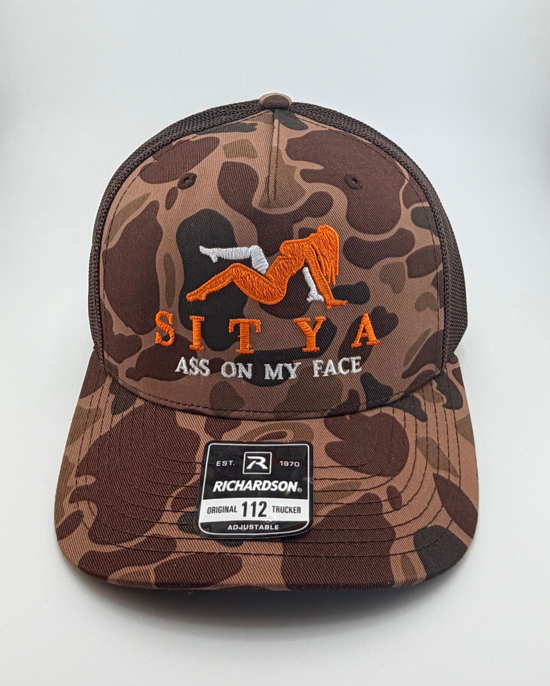 A brown camouflage trucker hat with an embroidered orange silhouette and text reading 