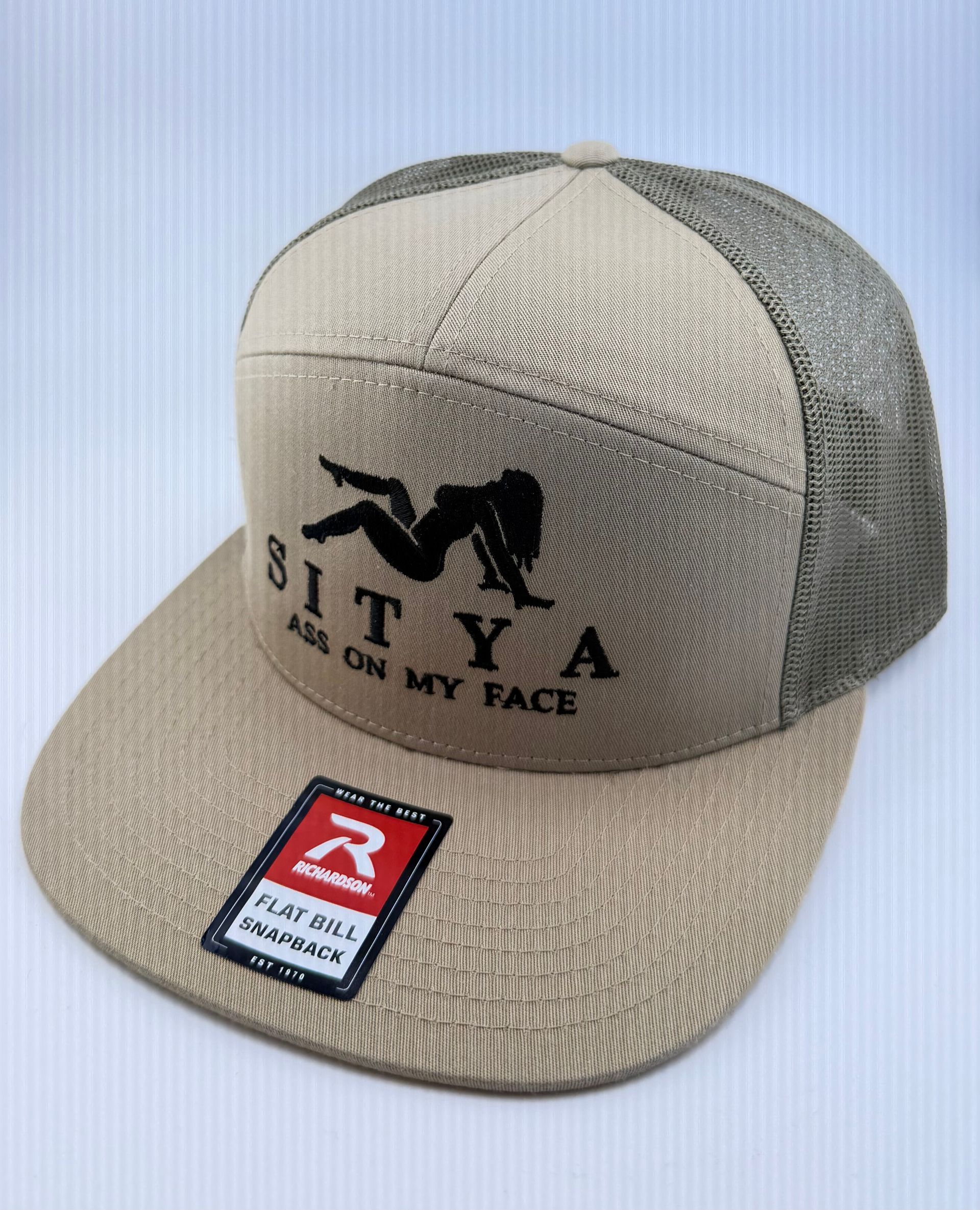 A tan and grey trucker-style baseball cap featuring a black silhouette graphic and text that reads 