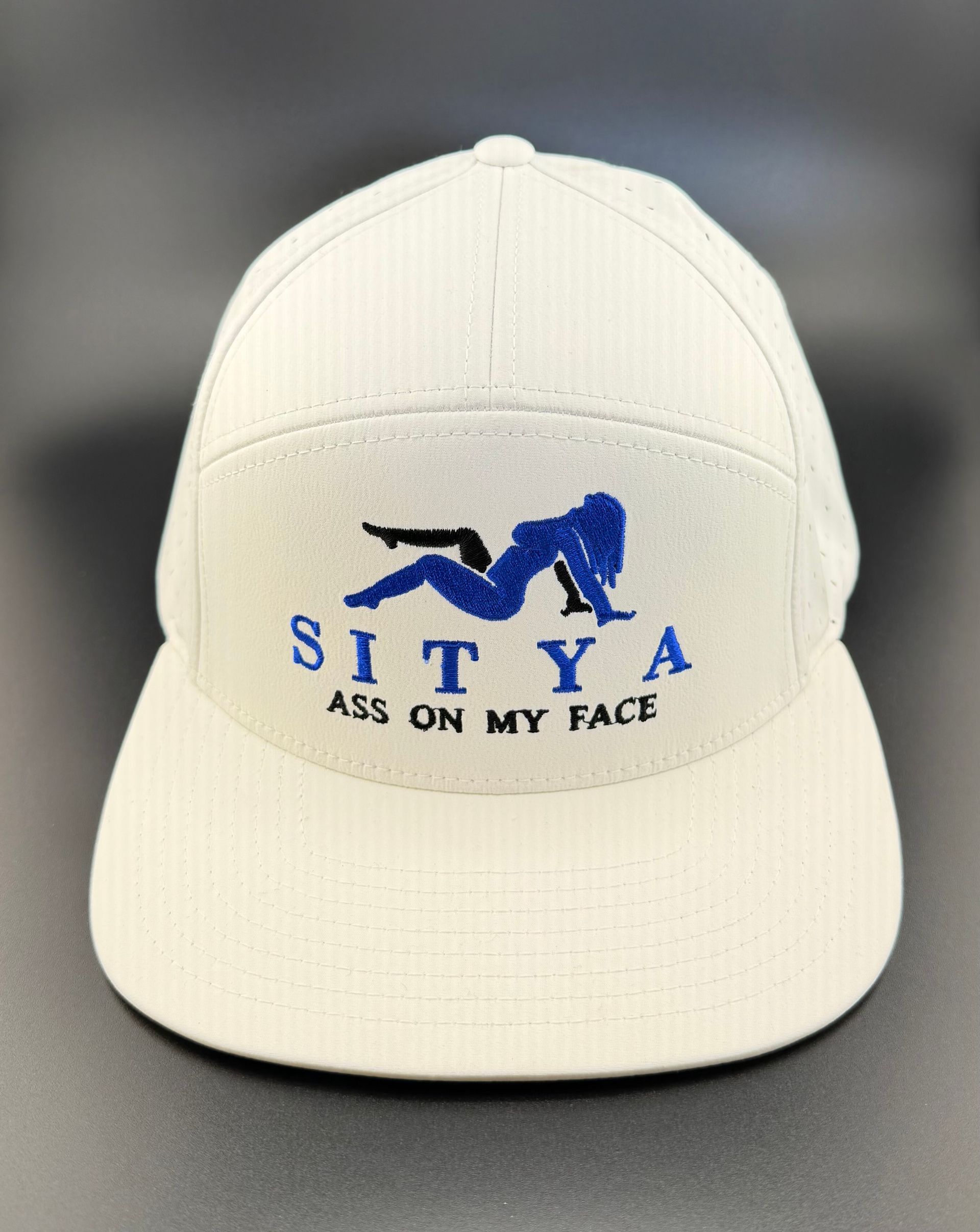 A light-colored baseball cap with an embroidered blue silhouette of a reclining figure and text reading