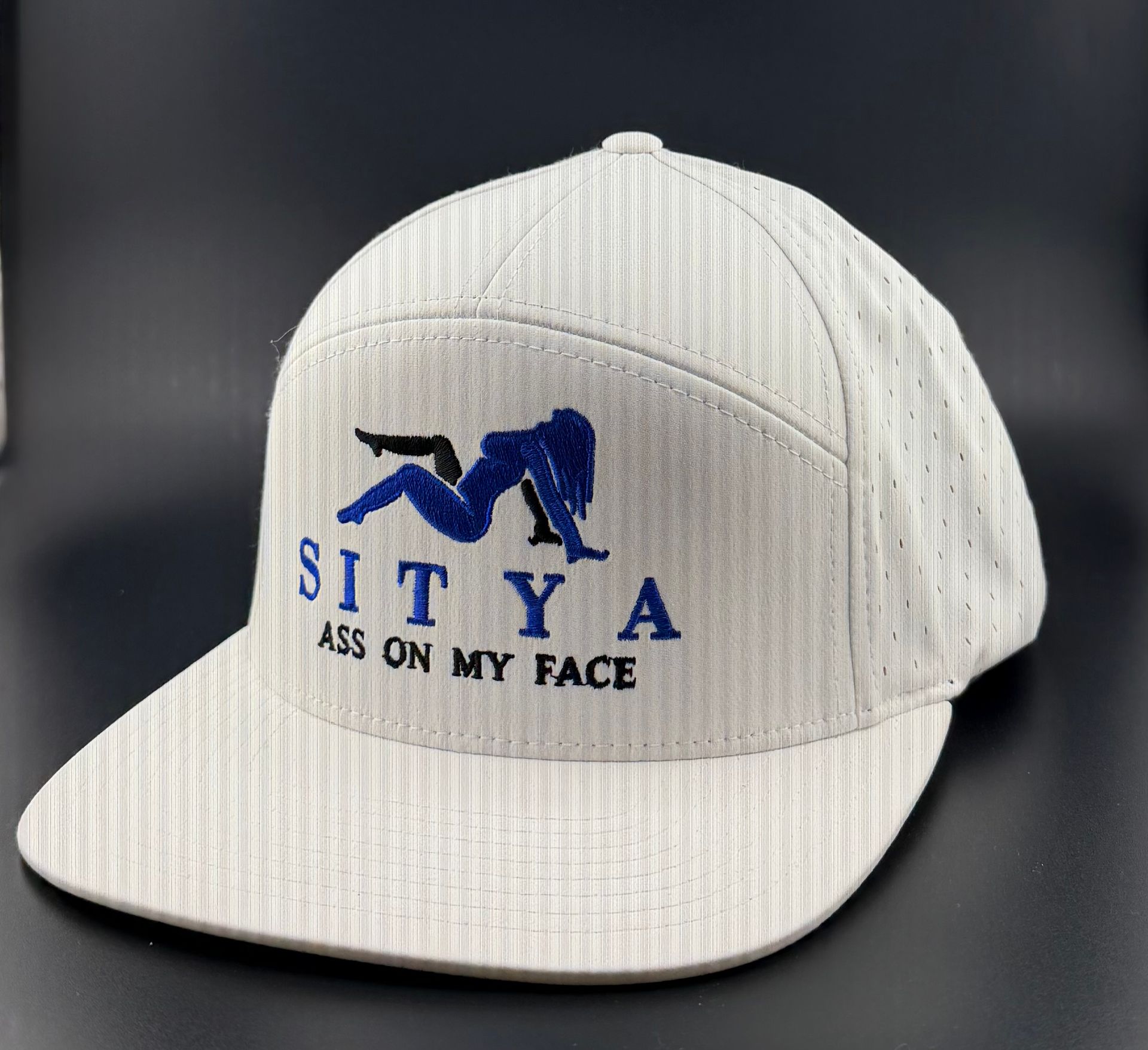A white baseball cap featuring a blue silhouette graphic above the text "SITYA" and "ASS ON MY FACE" in black.