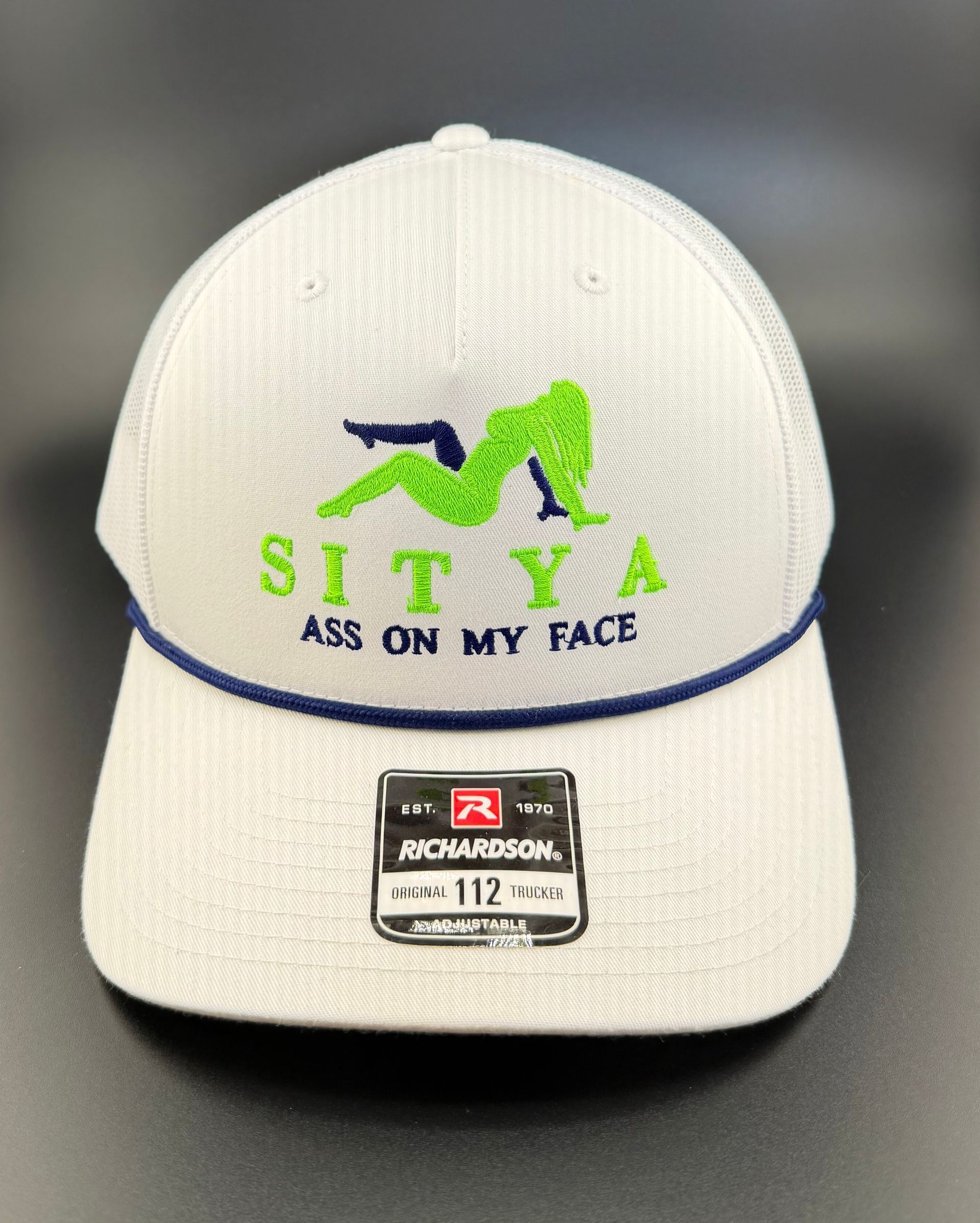 A white trucker hat with a dark blue brim rope. It features a green silhouette, the text 