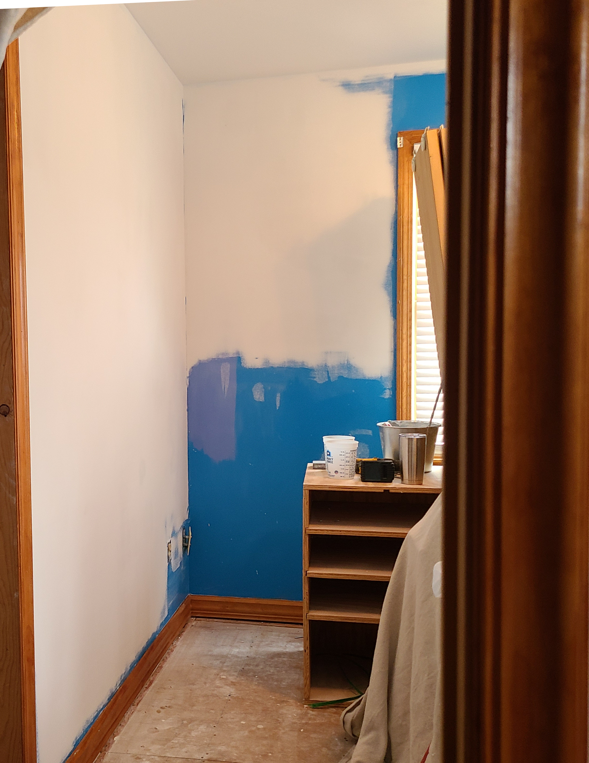Small room with white and blue walls, a wooden shelf, and a doorway on the left.