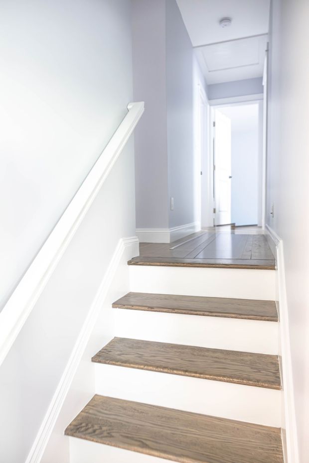Narrow white stairway with wooden steps leading to a bright hallway and open doorway.