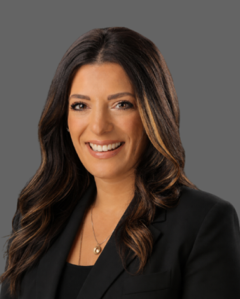 Professional headshot of a smiling woman with long dark hair, wearing a black blazer against a gray background