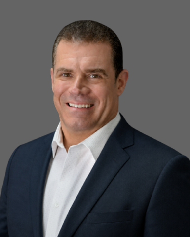 Studio portrait of a smiling man in a navy suit and white shirt on a gray background