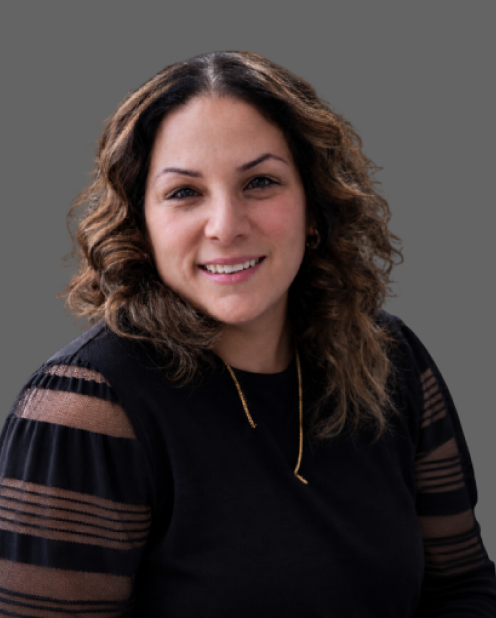 Smiling woman with curly dark hair wearing a black top against a gray background