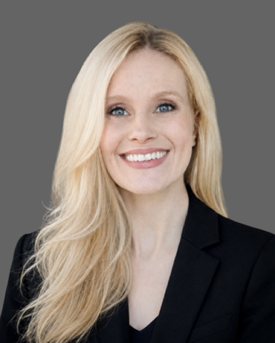Smiling blonde woman in a black blazer against a gray background