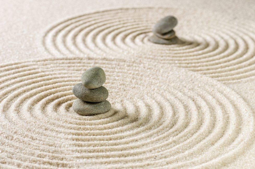 Two stacks of gray stones resting in the centers of circular, raked patterns in light-colored sand.