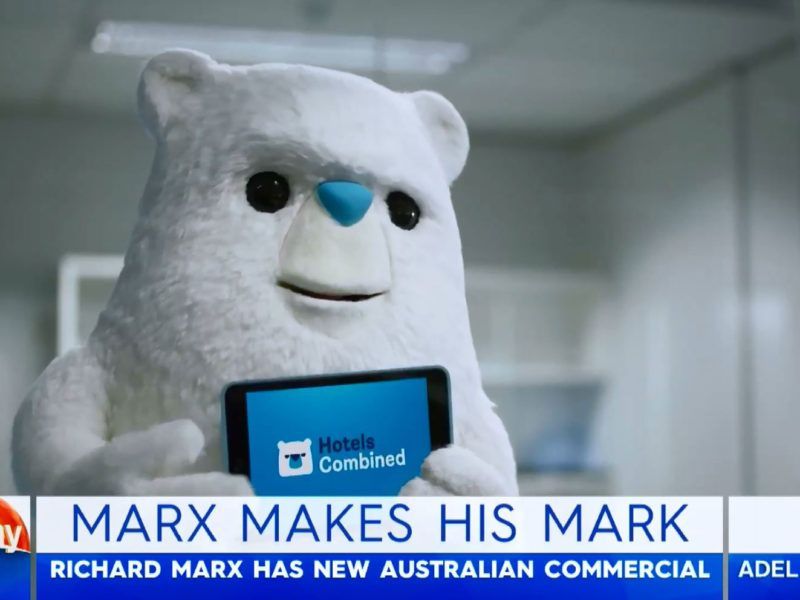The HotelsCombined mascot, a white bear with a blue nose, holds a tablet, with news headlines about Richard Marx below.