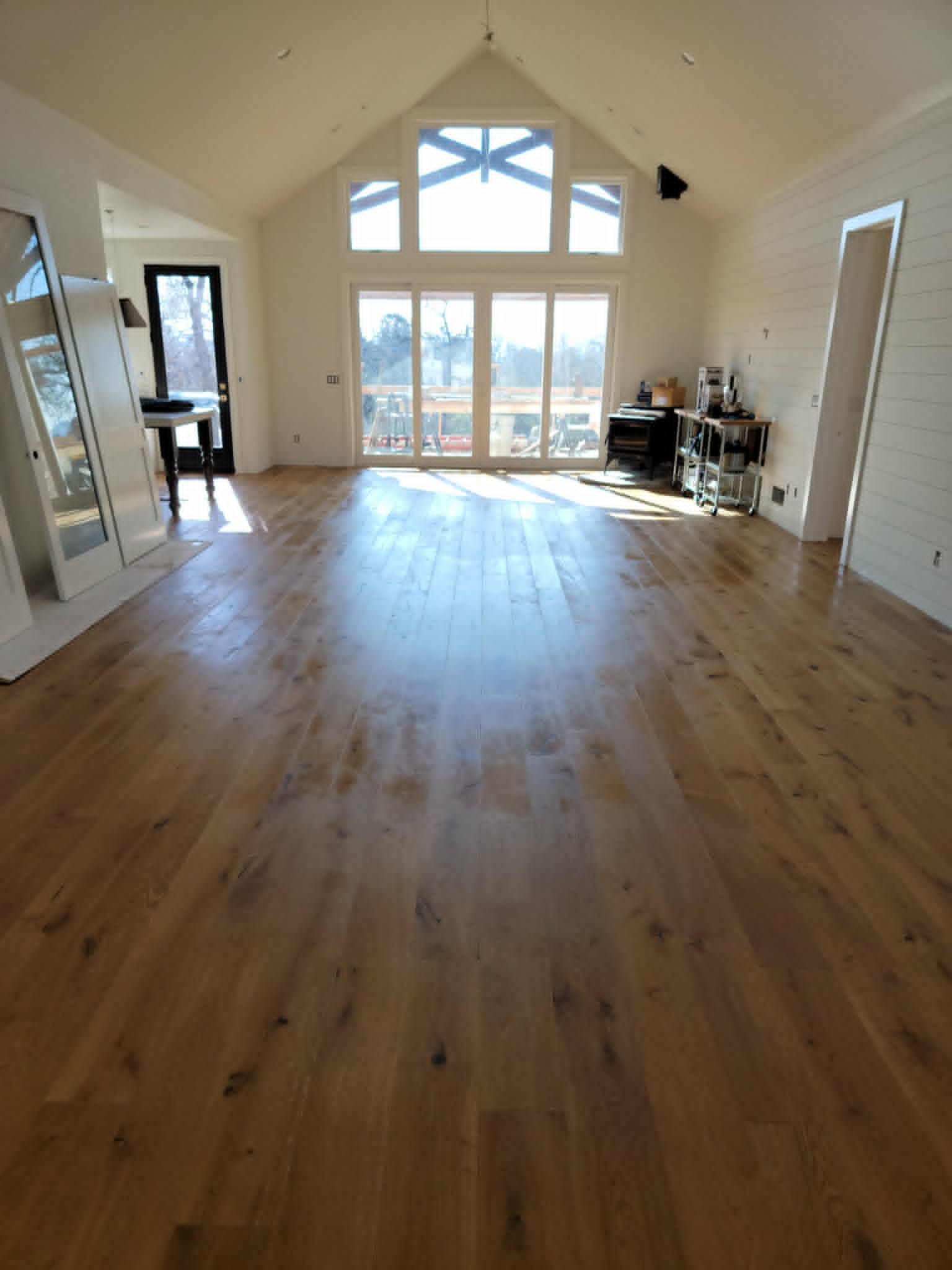 Bright empty living room with vaulted ceiling, large windows, and hardwood floors.