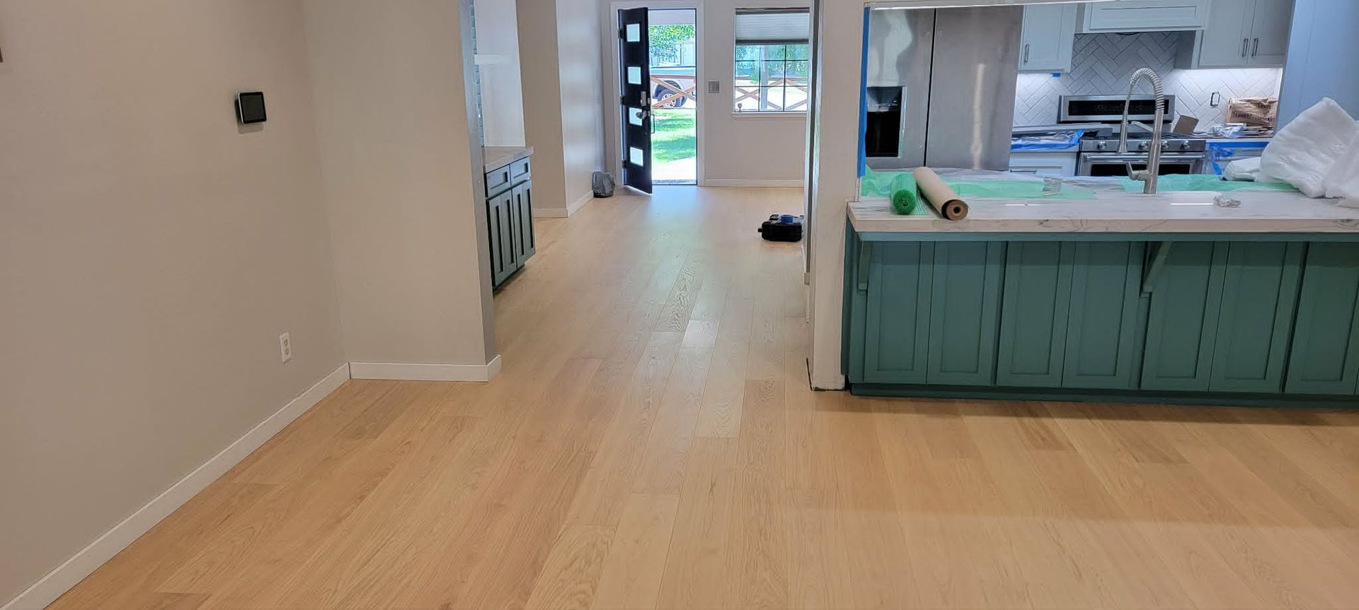 Modern kitchen with light wood floors, teal cabinets, and an open doorway to another room