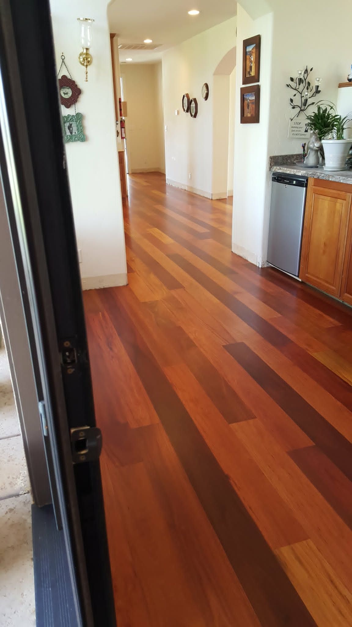Bright hallway with polished wooden floors, white walls, and a small cabinet with plants on the right.