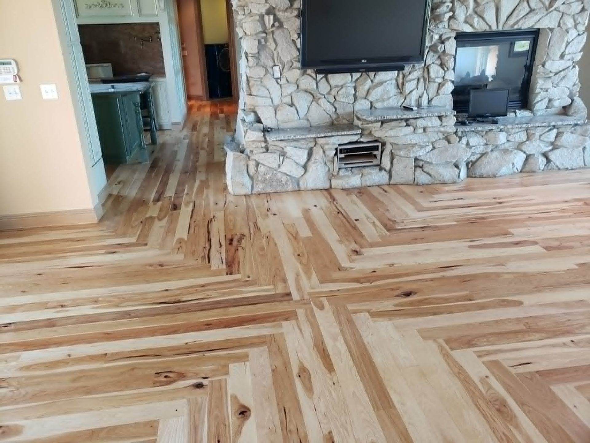 Wood floor with herringbone pattern in a living room, stone fireplace centered on the far wall.