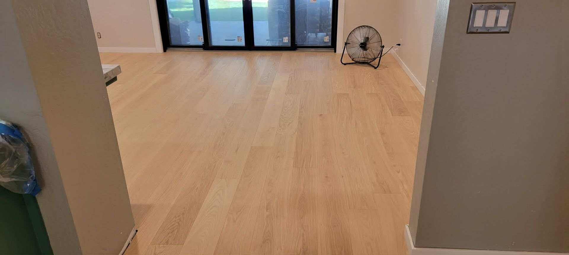 Empty room with light wood floor, gray walls, and glass doors at the far end.