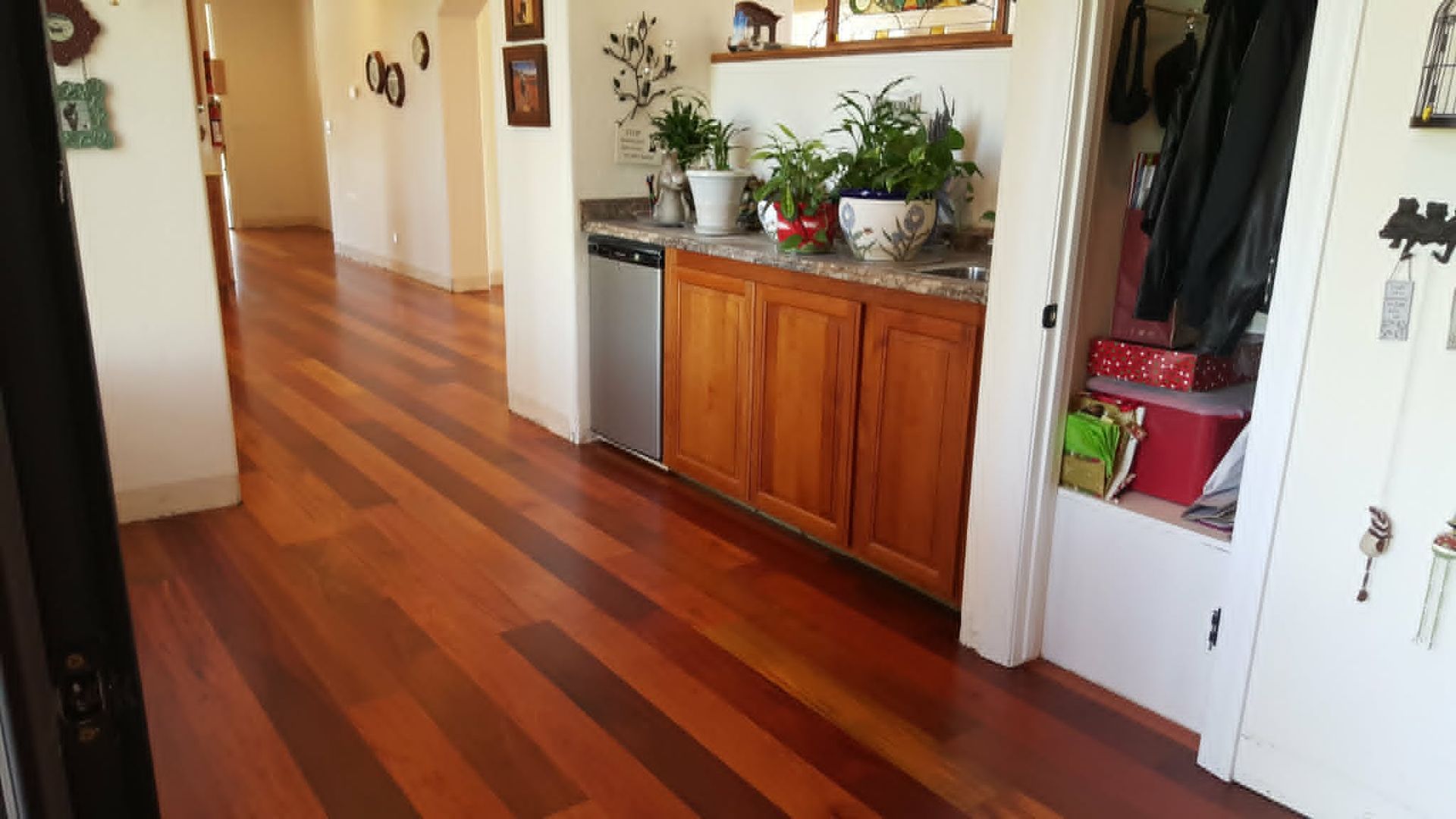 Hallway with polished wood floors, white walls, and a wooden cabinet topped with plants and decor.
