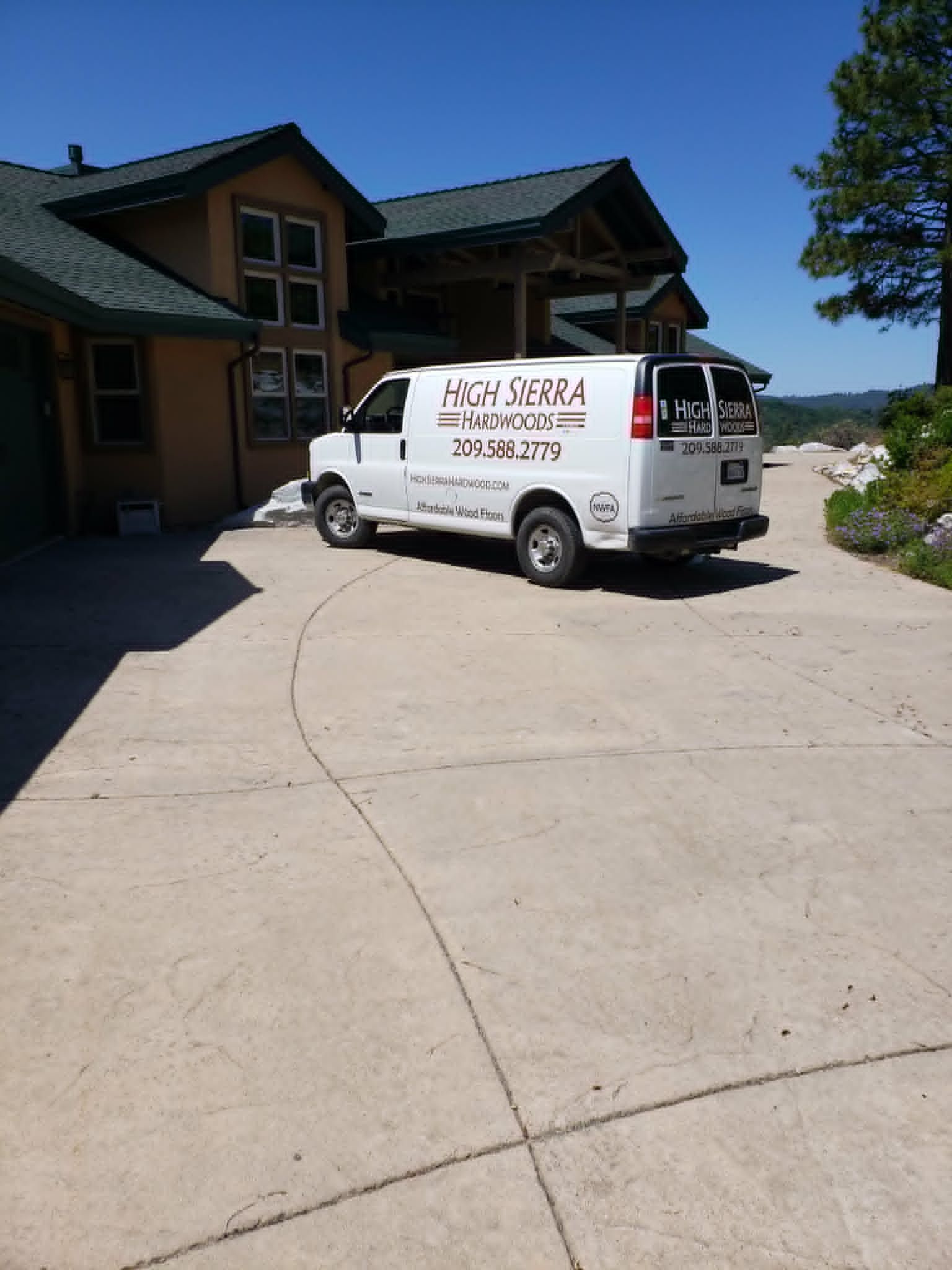 White service van parked on a driveway beside a large house on a sunny day.