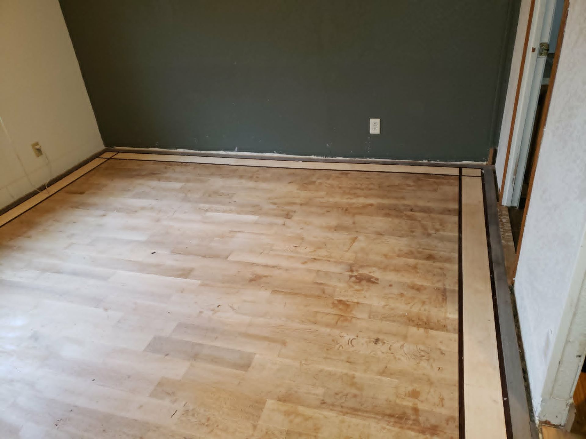 Empty room with light wood flooring, dark green wall, and a doorway on the right.