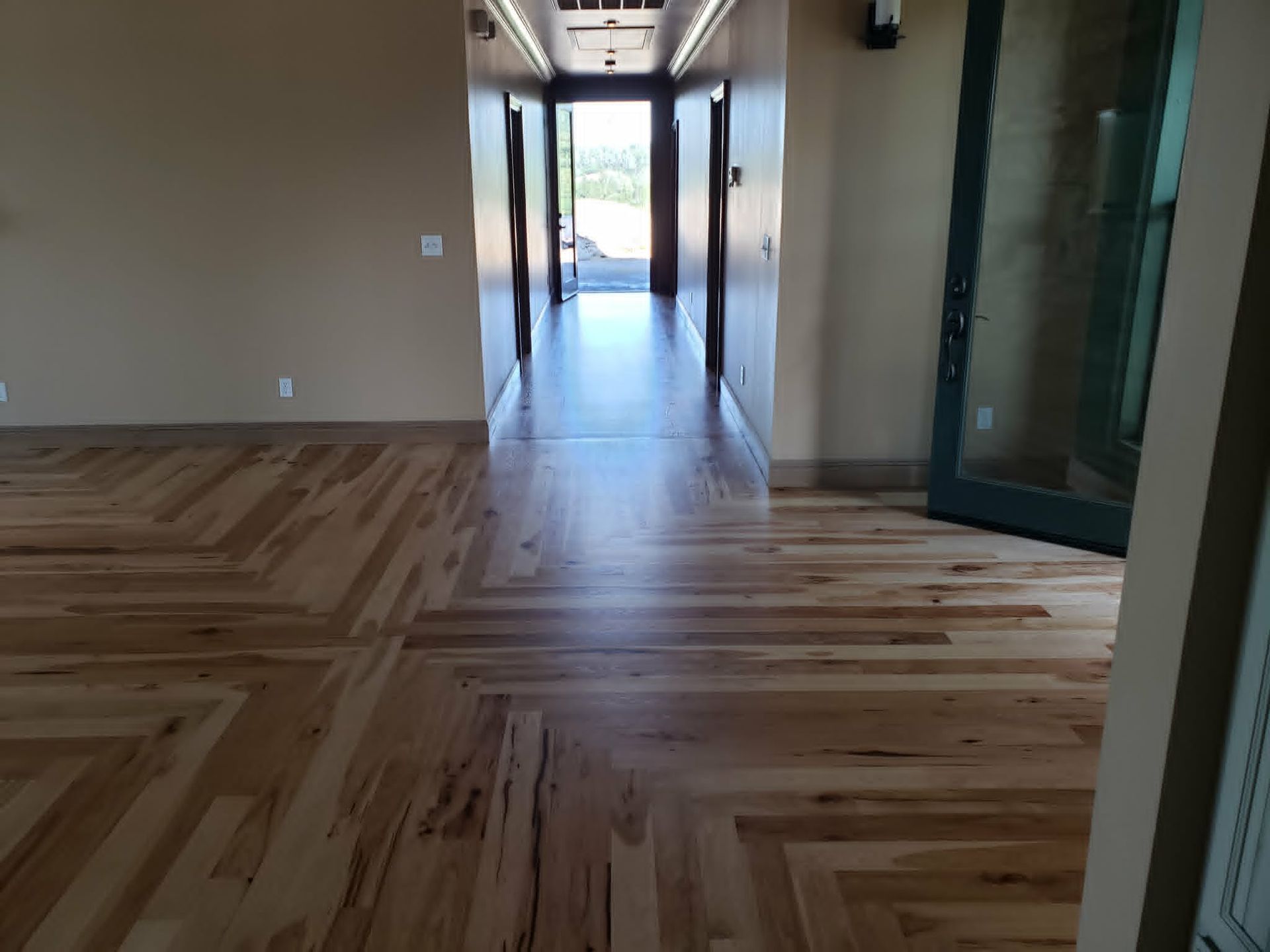 Empty hallway with patterned wood floor, beige walls, and bright light at the far end