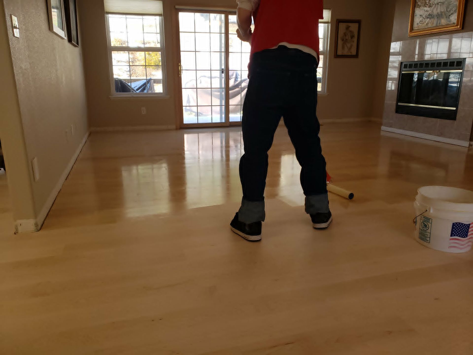 Person mopping a hardwood floor in a bright living room, with a bucket nearby.