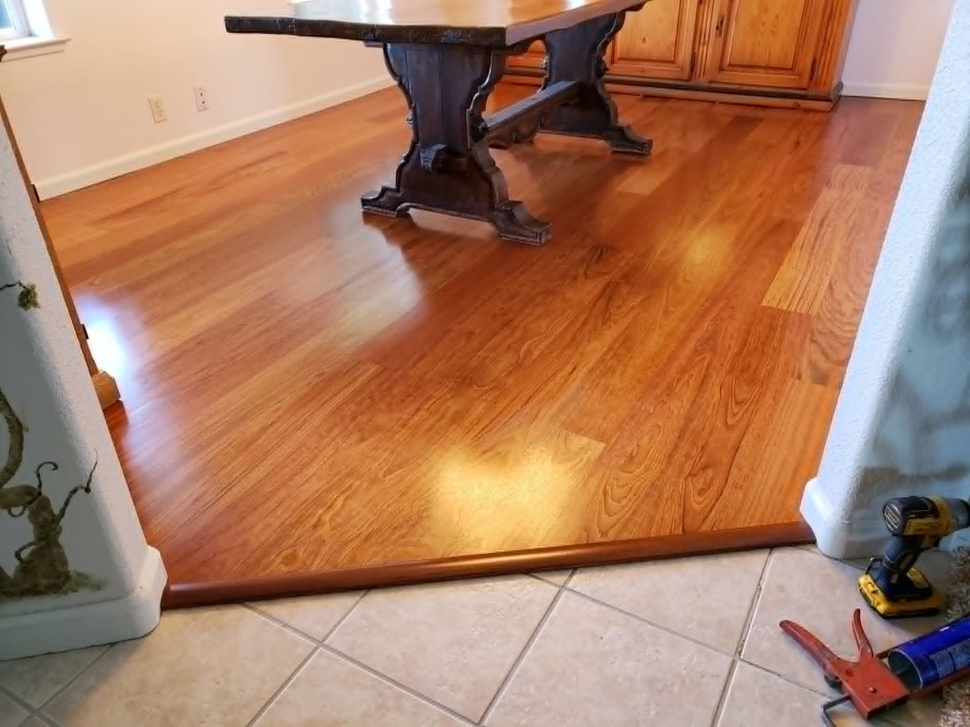 Dining room with a wooden table and glossy hardwood floor beside beige tile flooring.