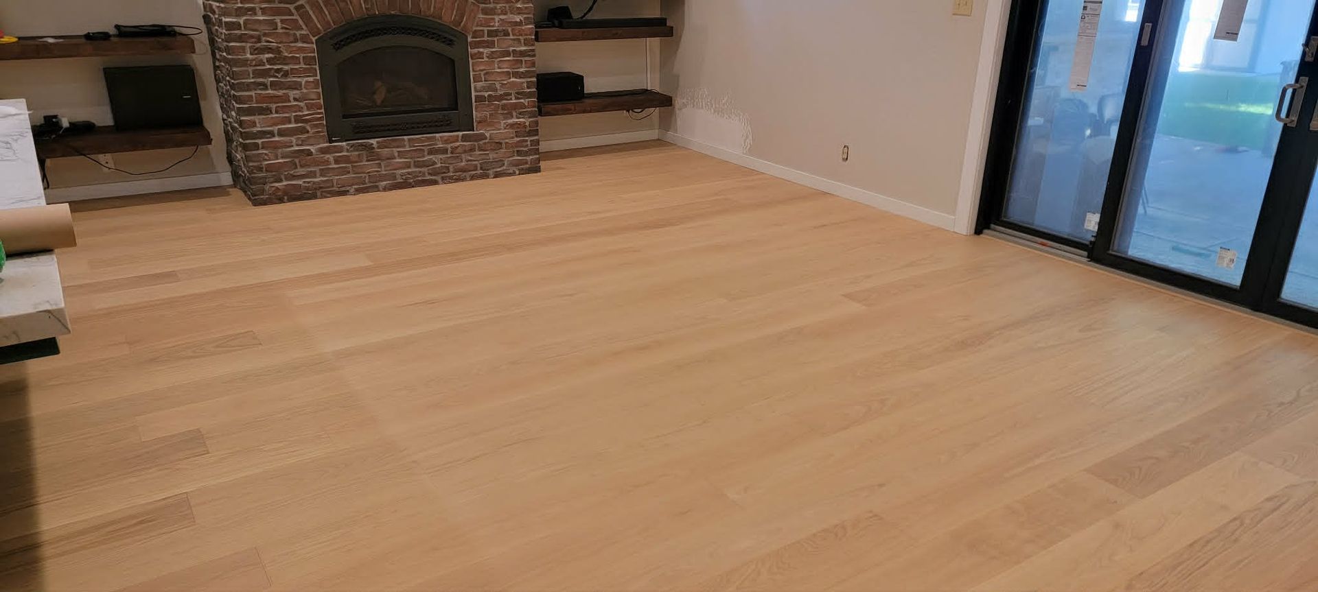 Empty living room with light wood floors, stone fireplace, and sliding glass doors.