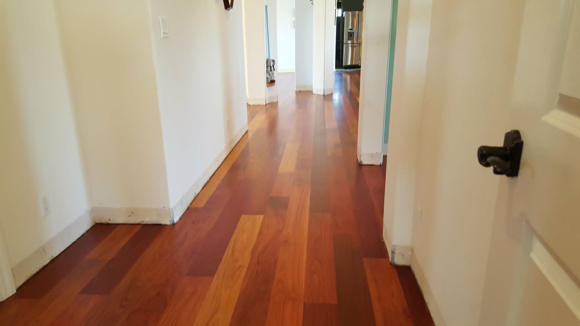Long hallway with polished wooden floors, white walls, and doors on both sides