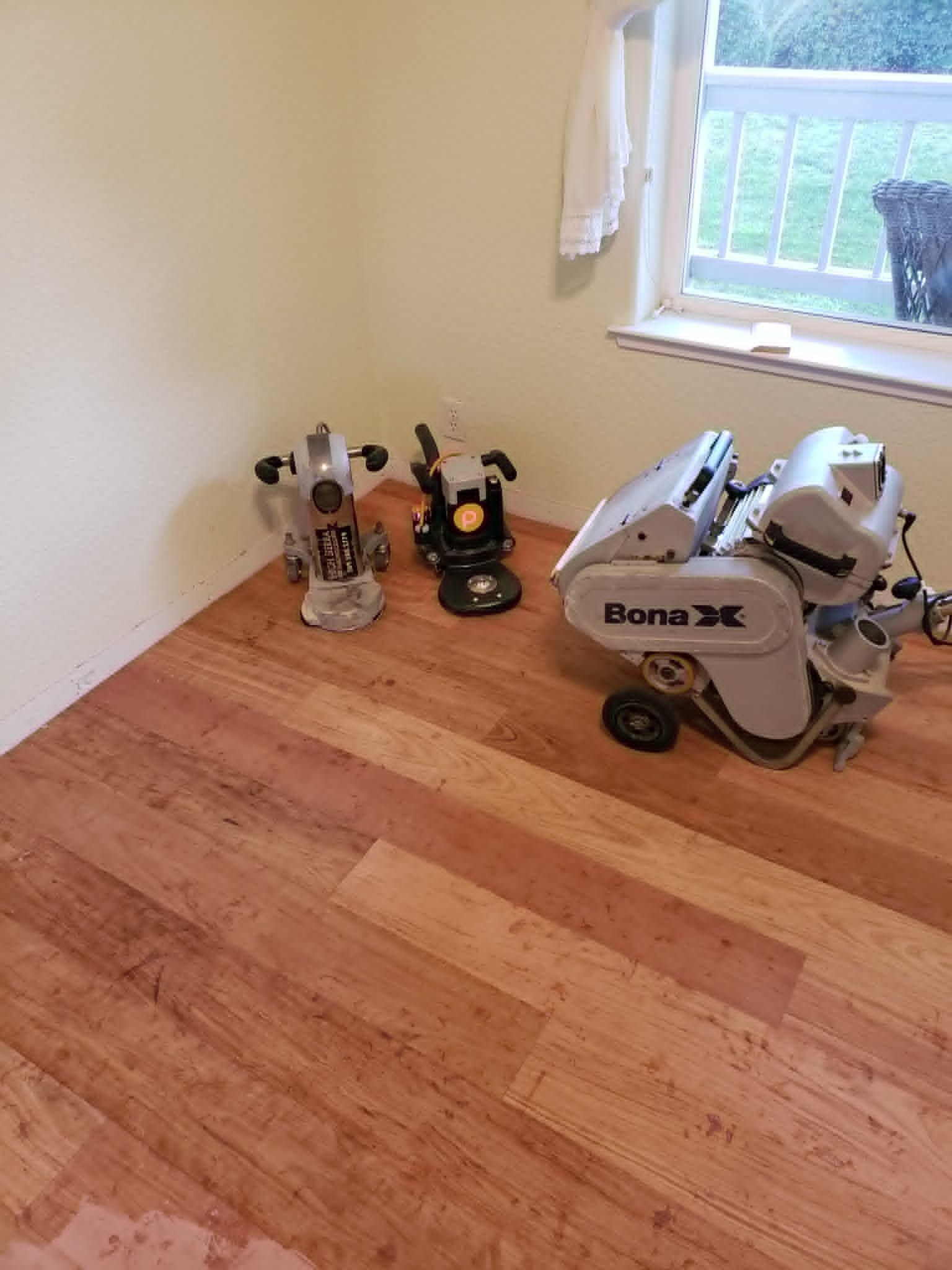 Empty room with hardwood floor, a window, and several tools and equipment stacked in one corner.