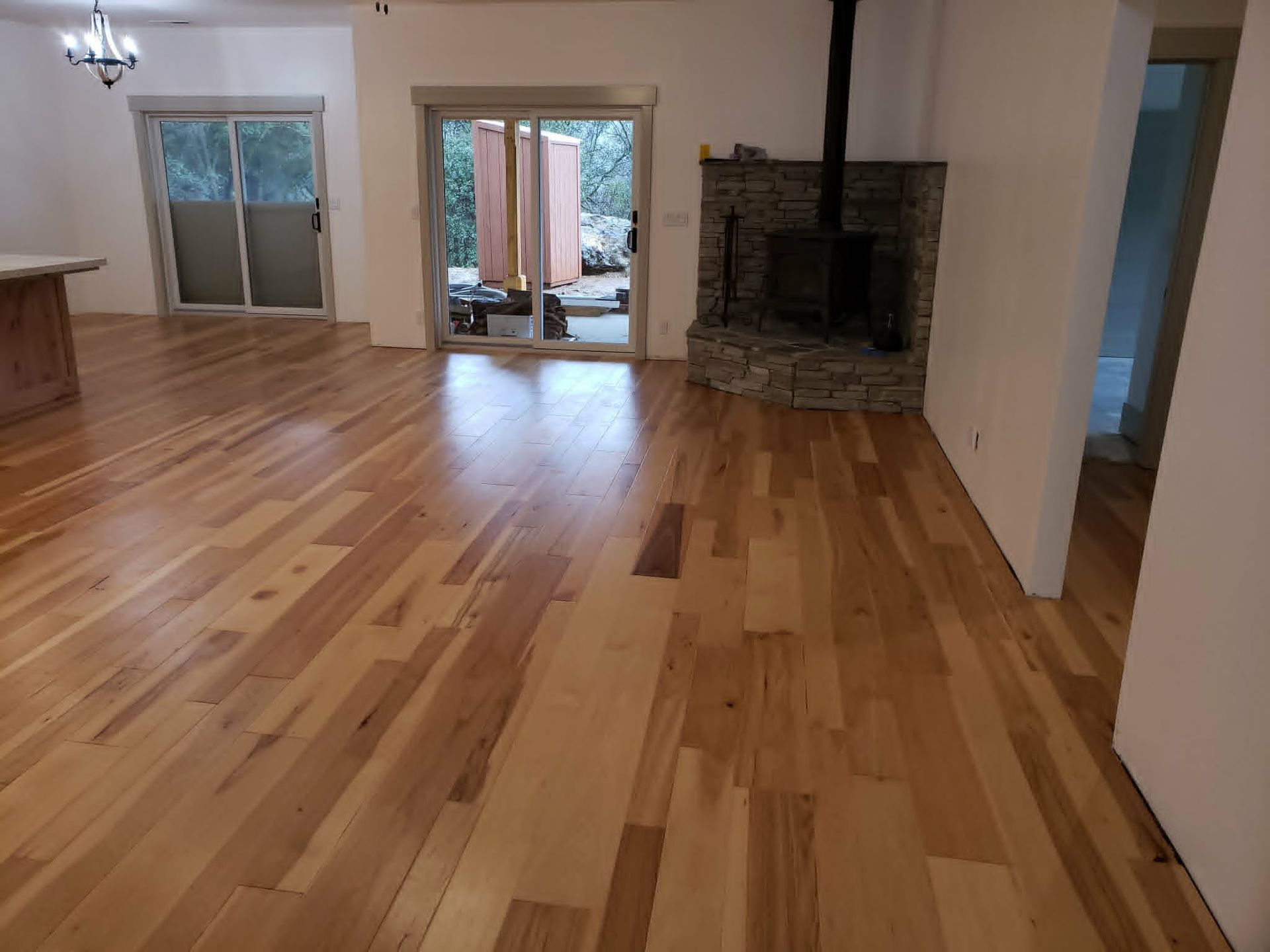 Empty living room with hardwood floors, stone fireplace, and sliding glass doors to a patio.