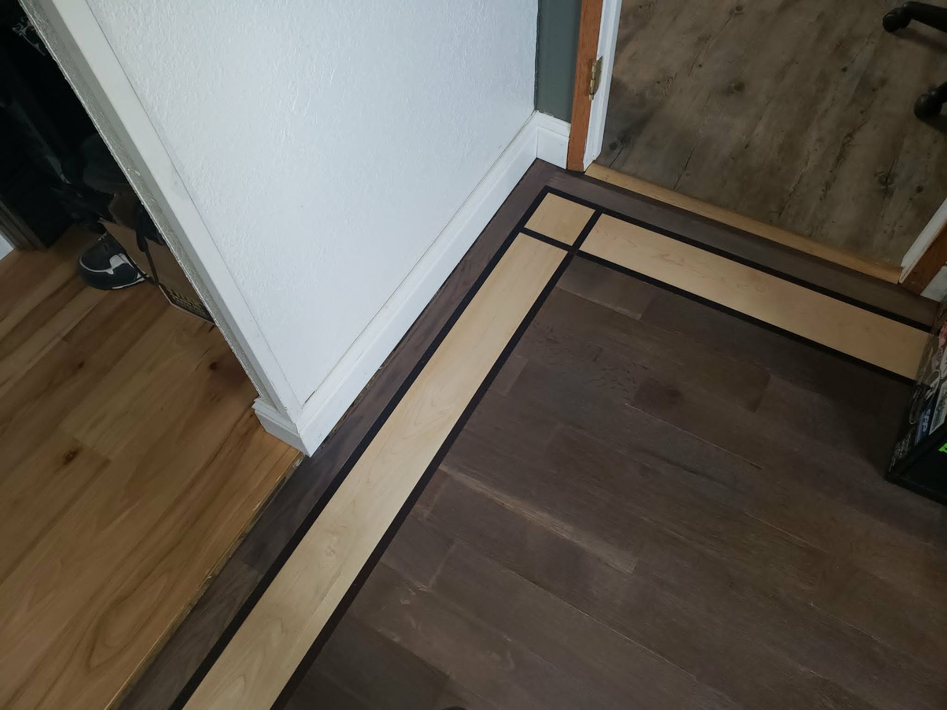 Wooden floor with a corner rug beside a white wall and doorway