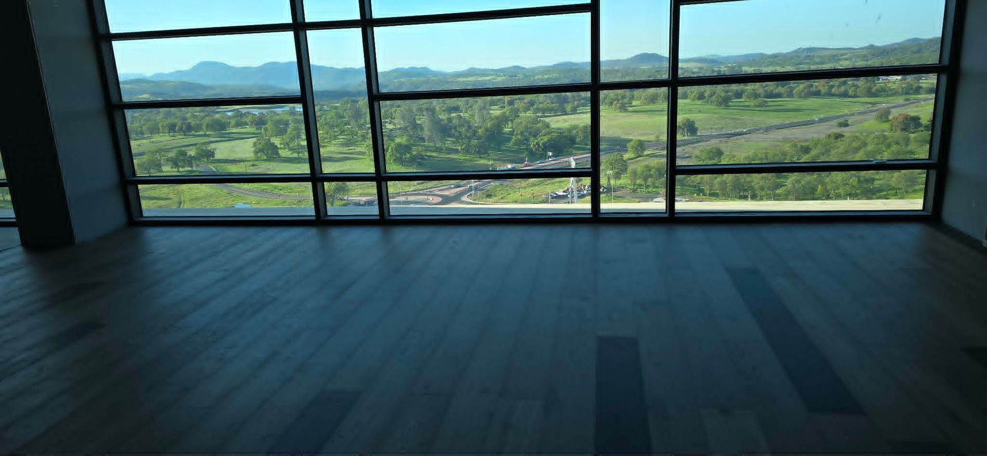 Empty room with large windows overlooking a green valley and distant mountains