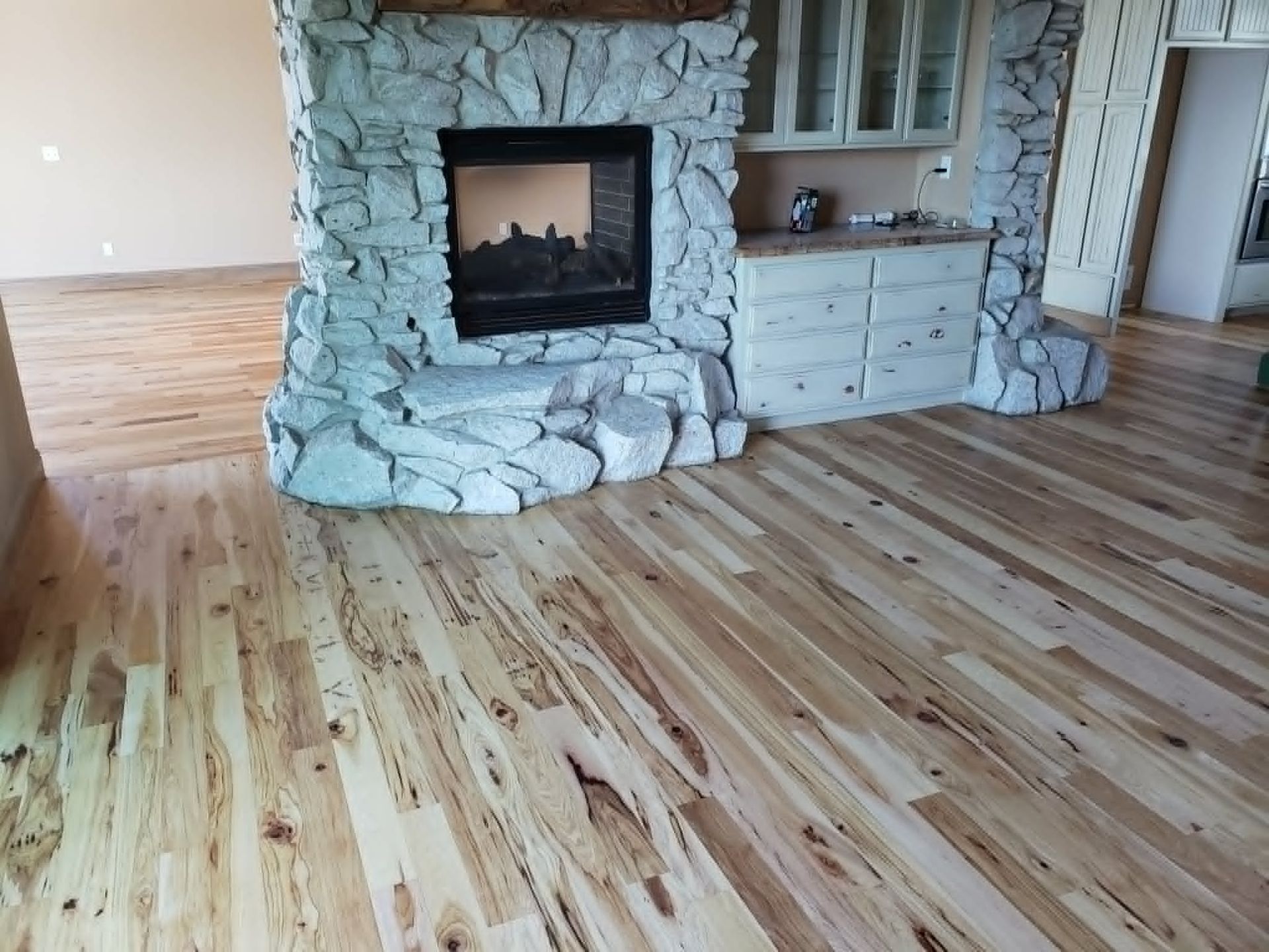 Empty room with wide wood plank floor and a stone fireplace with built-in cabinets
