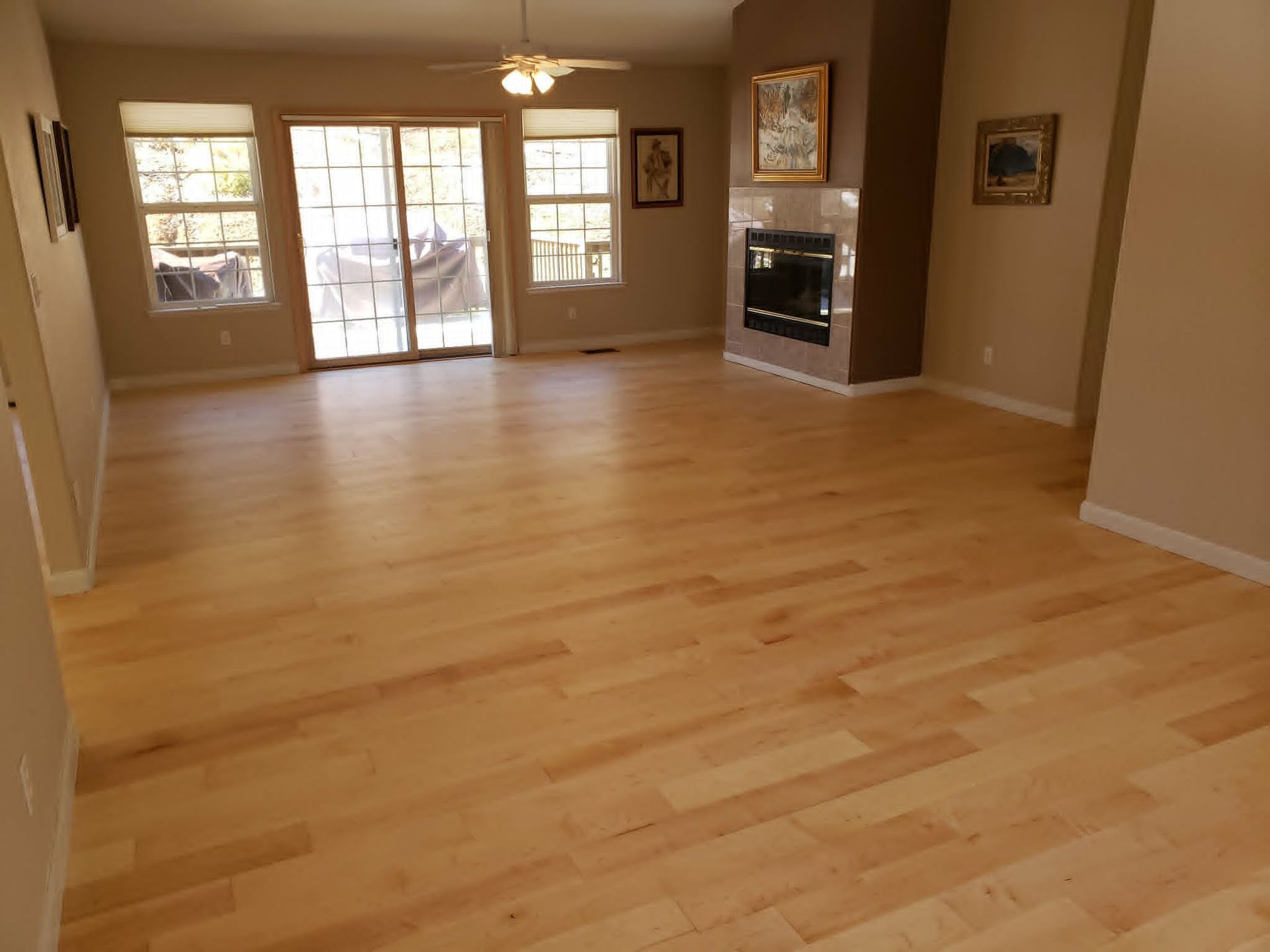 Empty living room with light hardwood floors, beige walls, fireplace, and French doors to a patio.
