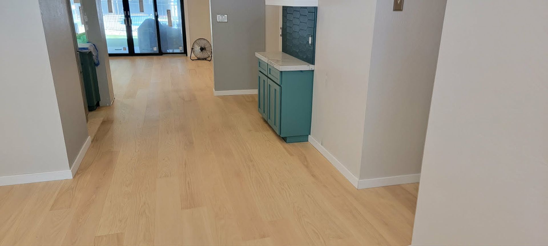 Empty modern hallway with light wood floors, white walls, and teal cabinets near a doorway.