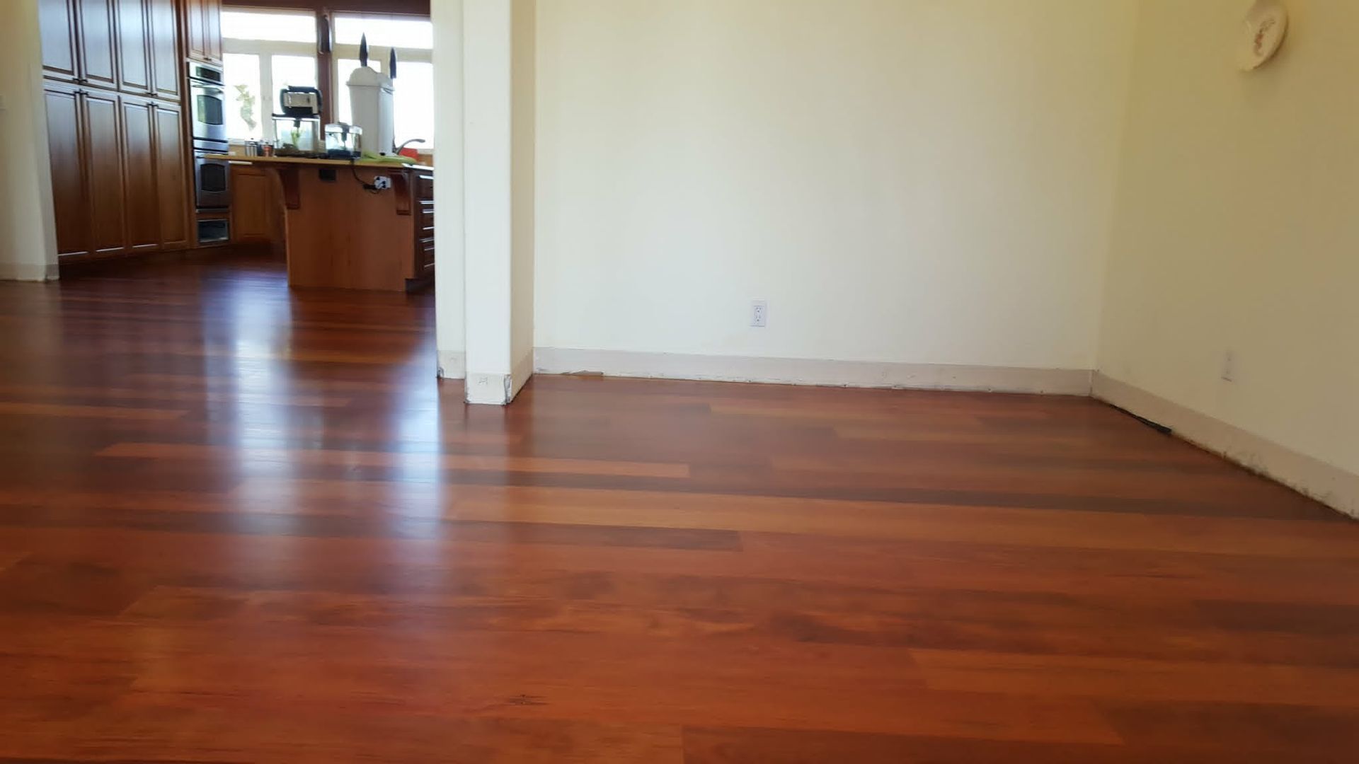 Empty room with polished hardwood floor and open doorway to a kitchen area