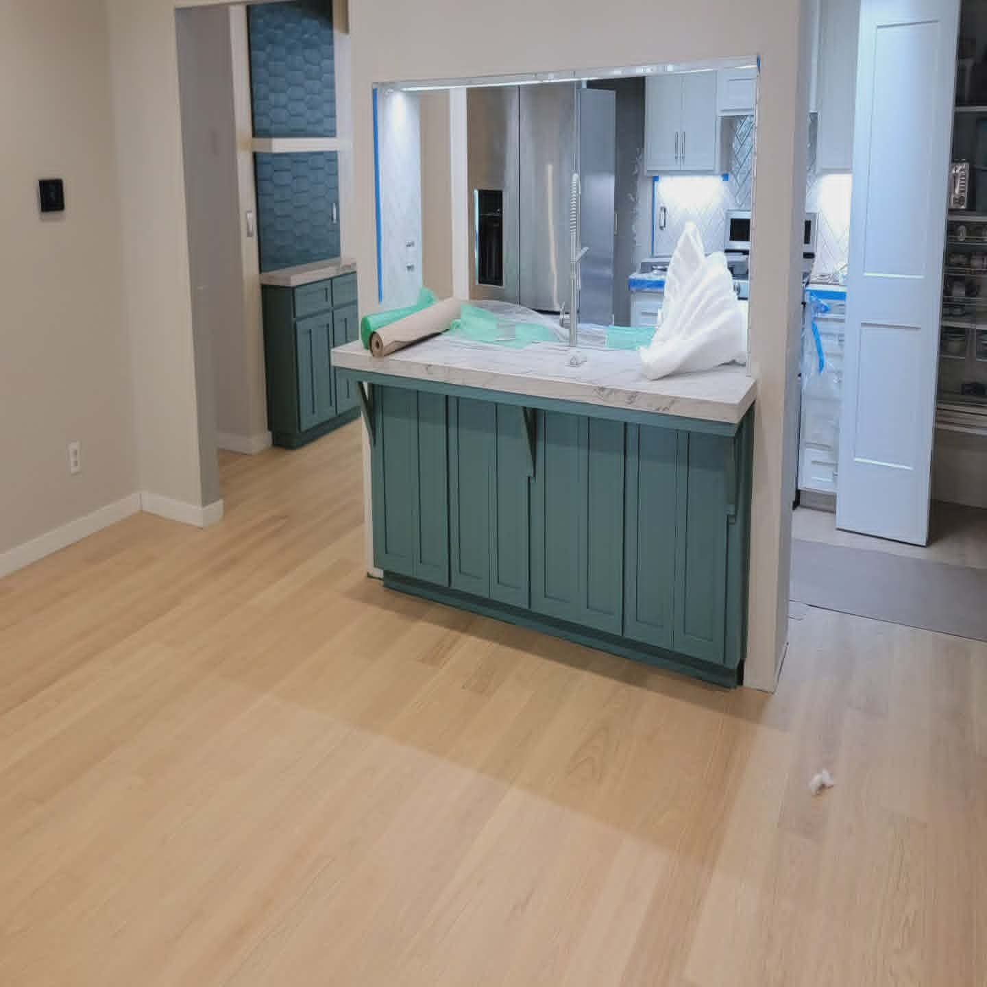 Empty kitchen with teal island cabinets, light wood floors, and mirror backsplash under renovation