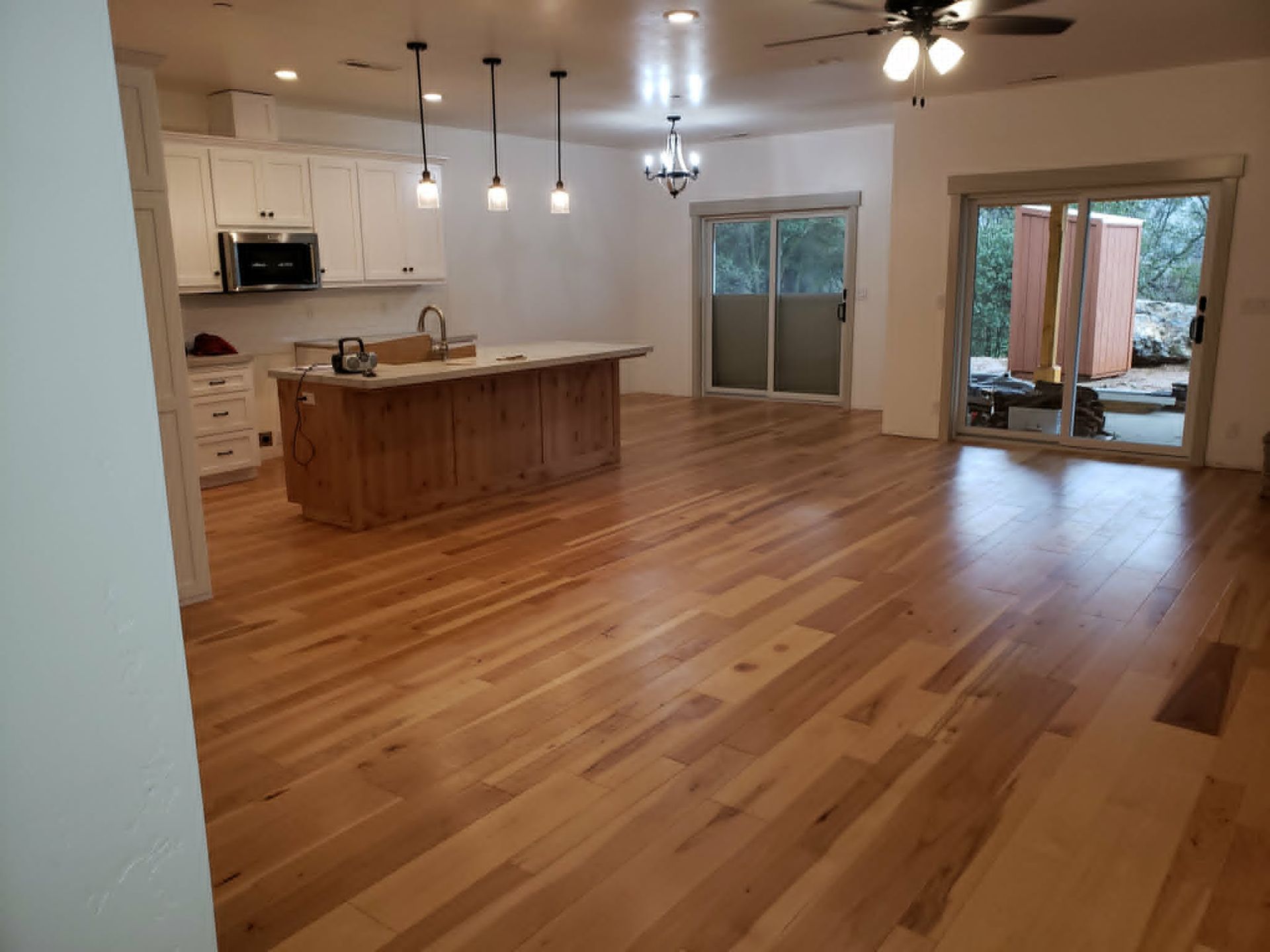 Open-plan kitchen and living room with wood floors, island, pendant lights, and sliding glass doors to a patio