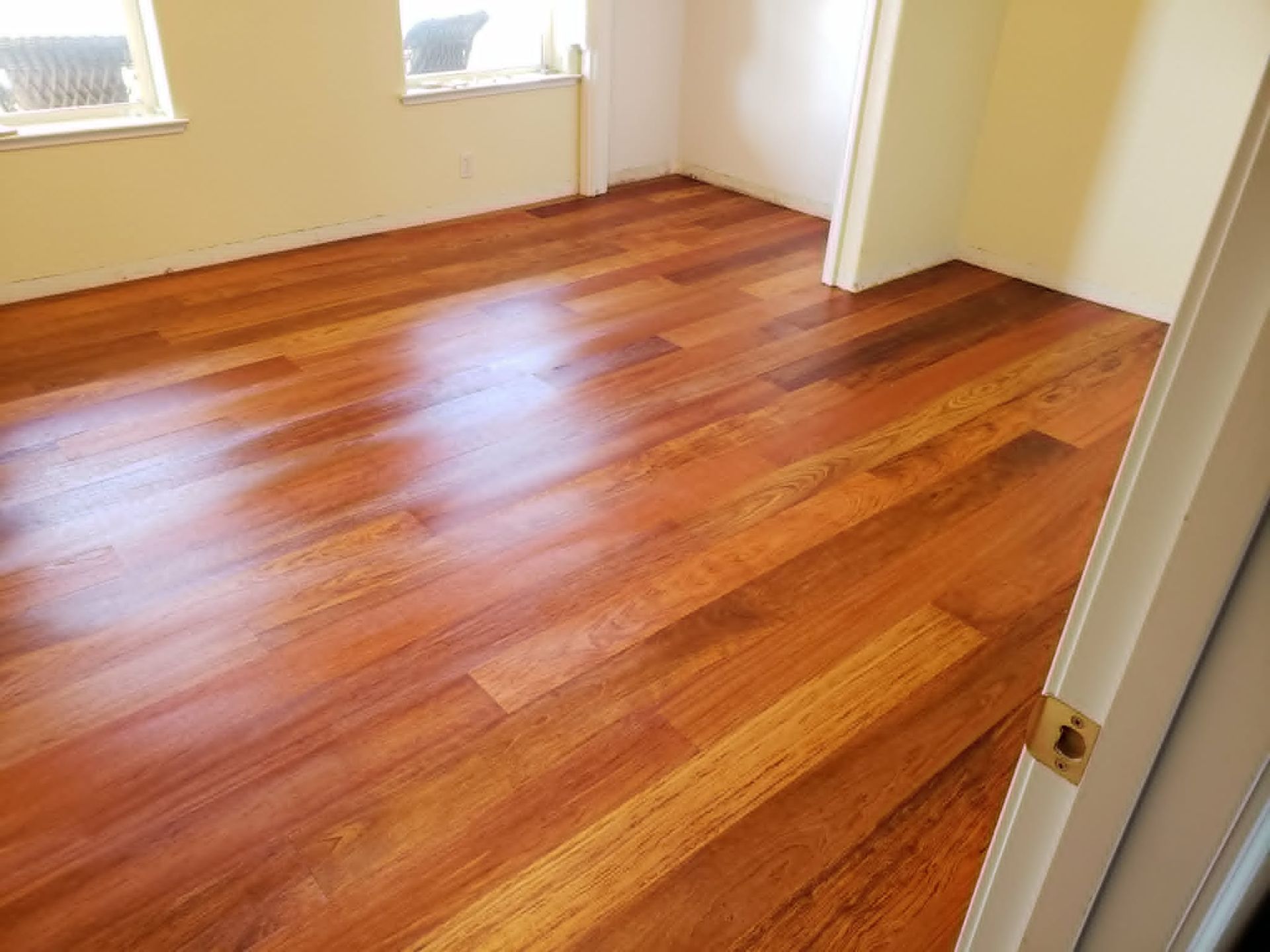 Empty room with glossy hardwood floors and white walls, viewed from a doorway.