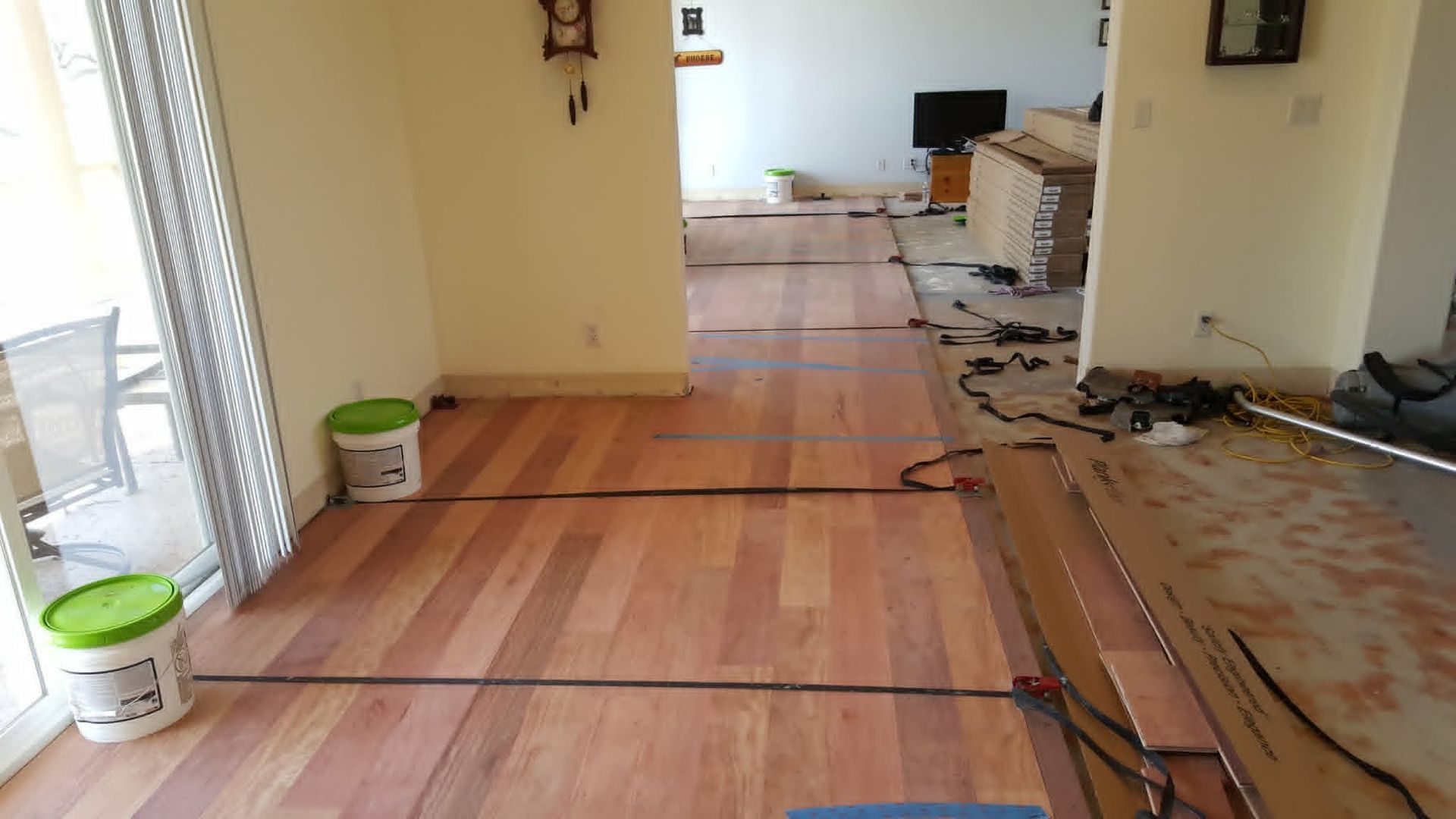 Empty room under renovation with stripped flooring, scattered tools, and exposed floorboards.